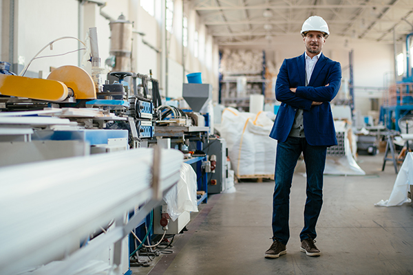 Businessman with a construction site helmet standing in an industrial hall next to machines