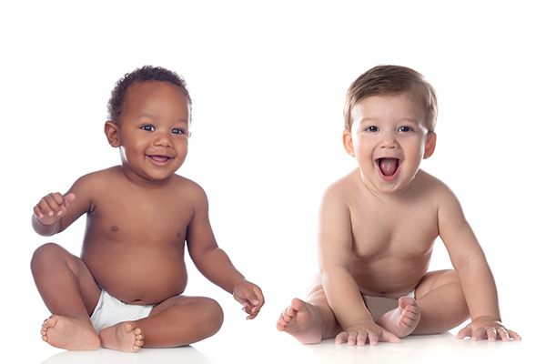 Two laughing toddlers sitting on the floor wearing a diaper