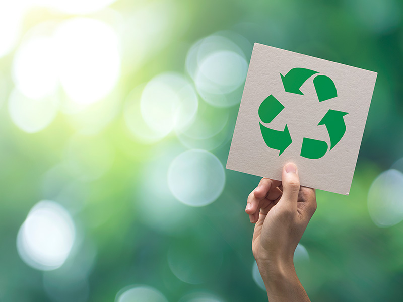 Eine Hand welche das Recycling-Symbol auf einem Stück Papier hoch hält